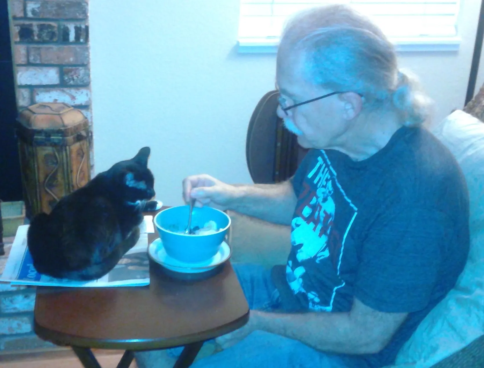 A picture of Jim eating out of a bowl with his cat watching.